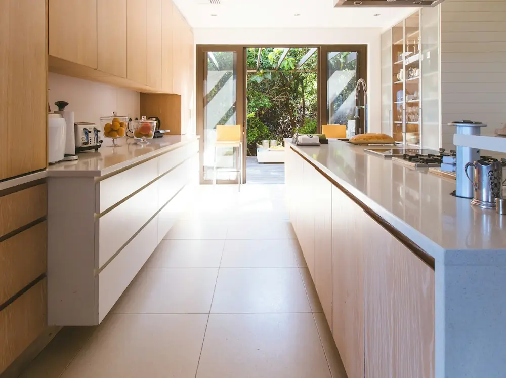 An empty kitchen with a long island, daylight coming through the far doors